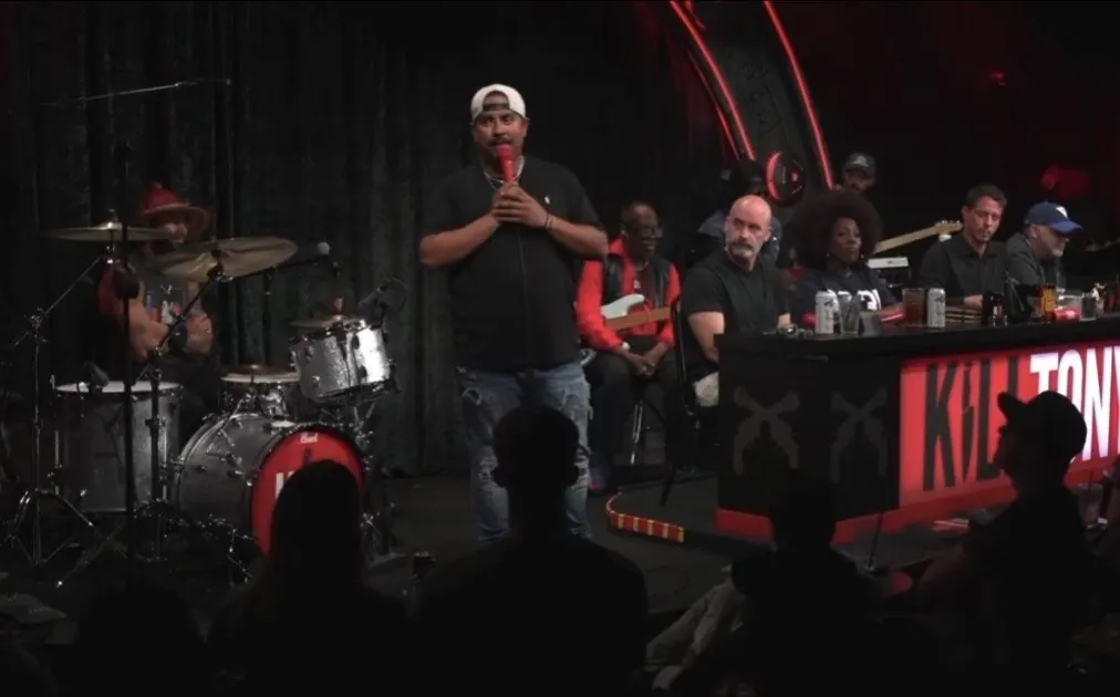 Chris Longoria on stage at Kill Tony, with the panel behind him